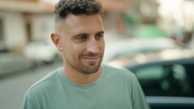 Young hispanic man smiling confident looking to the side at street