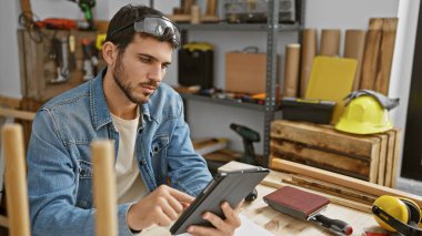 Sakallı yakışıklı İspanyol bir adam marangozluk atölyesinde tablet üzerinde çalışıyor..