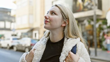 Düşünceli genç bir kadın güneşli bir şehir sokağına bakıyor. Güzelliği ve kentsel keşifleri somutlaştırıyor..