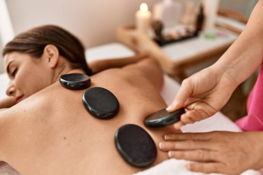 Genç ve güzel İspanyol kadın güzellik salonunda sıcak taş masajı yaptırıyor.