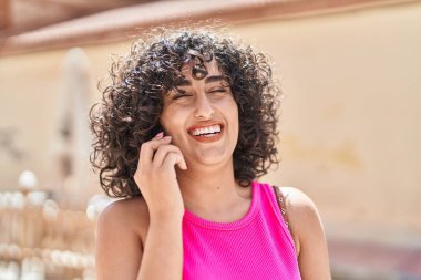 Orta Doğulu genç bir kadın gülümsüyor oyun odasında akıllı telefondan konuşuyor.