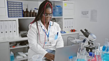 Odaklanmış Afrikalı Amerikalı kadın bilim adamı. Laboratuvarda bilgisayarında ciddi tıbbi araştırmalara dalmış. Güzel bir yetişkinin portresi..