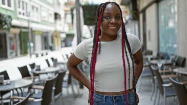 Kendinden emin Afrikalı Amerikalı kadın, neşe içinde güneşli bir kahve dükkanının terasında dikiliyor.