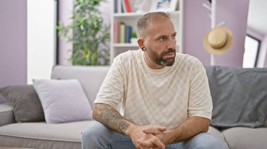 Yakışıklı bir genç, şüpheci bir adam, evdeki oturma odasındaki kanepede oturuyor, ciddi, düşünceli bir ifadeyle endişe içinde yan tarafa bakıyor.