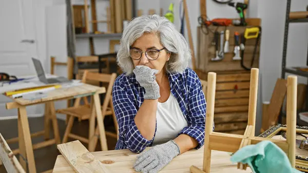 一个成熟的女人在一个木匠工具环绕的木匠工作室里若有所思地停下来 — 图库照片
