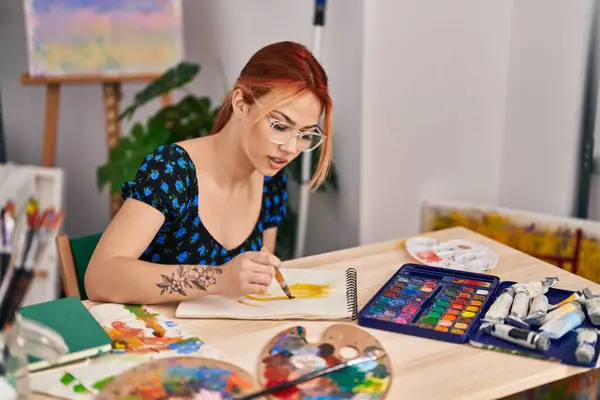 Young caucasian woman artist drawing on notebook at art studio