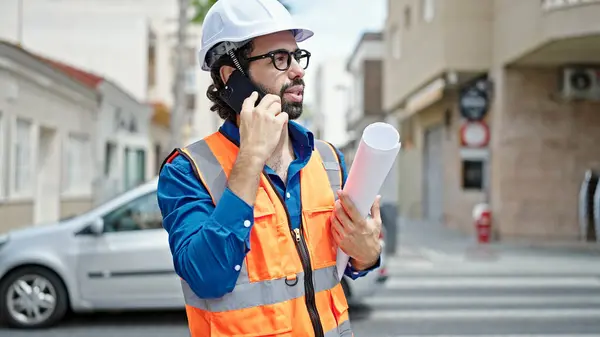 Young Hispanic Man Architect Holding Blueprints Talking Smartphone Construction Place — Stock Photo, Image