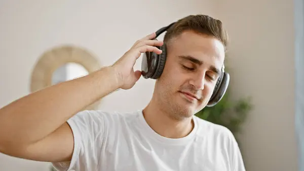 一个心满意足的年轻人喜欢在明亮的客厅里用耳机听音乐 — 图库照片