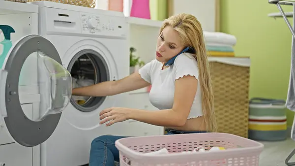 洗濯室でスマートフォンで話している若い金髪の女性 — ストック写真