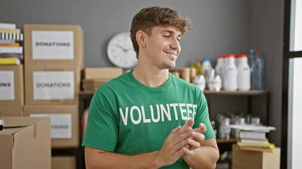 Handsome young hispanic man volunteering at a charity center, confidently clapping and smiling in applause, making a difference in his community