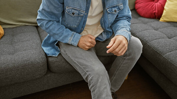 A young, bearded man in casual clothing relaxing on a modern couch in a stylish living room