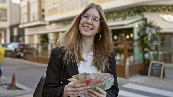 Smiling woman holding norwegian kroner on a city street, embodying youth, beauty, and urban lifestyle.