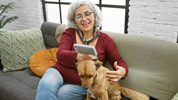 Kapalı bir koltukta köpek beslerken telefonuna gülümseyen gri saçlı olgun bir kadın..