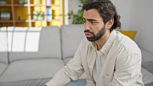 Молодой латиноамериканец сидит дома на диване и говорит: