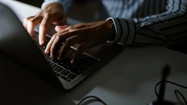 Close-up of a man\'s hands typing on a laptop keyboard in a dimly lit office setting, conveying a sense of business, technology, and focused work.