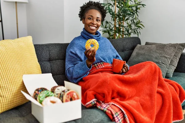 Afro-Amerikalı kadın kahvaltısını evde, kanepede yapıyor.