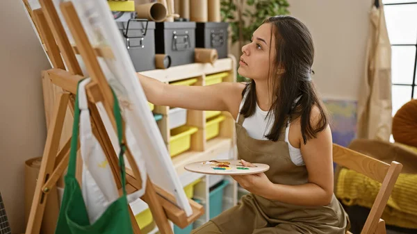 美しく 焦点を当てた若いヒスパニック系女性アーティストが椅子に座り 創造性に浸り アートスタジオで屋内で絵を描く — ストック写真