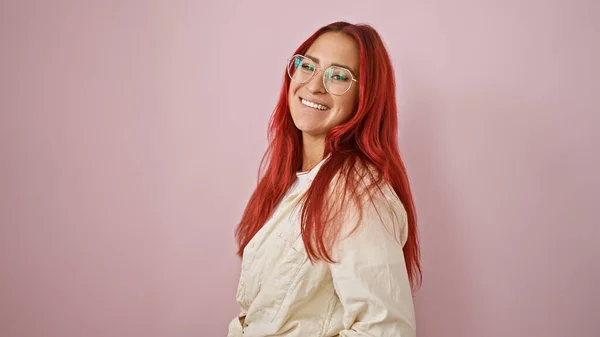 Joyous young redhead woman exuding confidence, flashing a radiant smile, standing casually over an isolated pink background, her energy infectious.