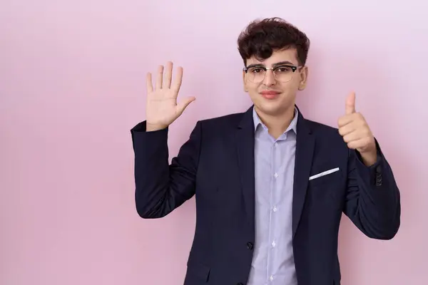 Young non binary man with beard wearing suit and tie showing and pointing up with fingers number six while smiling confident and happy.