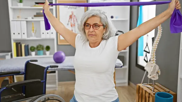Mature Woman Exercising Resistance Band Rehab Clinic Alongside Wheelchair — Stock Photo, Image