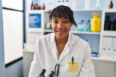 Young beautiful latin woman scientist smiling confident standing at laboratory