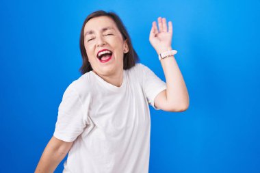 Orta yaşlı İspanyol kadın mavi arka planda dans ediyor mutlu ve neşeli, hareketli ve kendinden emin müzik dinliyor. 