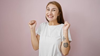 İzole edilmiş pembe arka planda kutlama yaparken kendinden emin gülümseyen genç kadın.