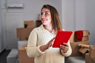 Young beautiful hispanic woman smiling confident using touchpad at new home