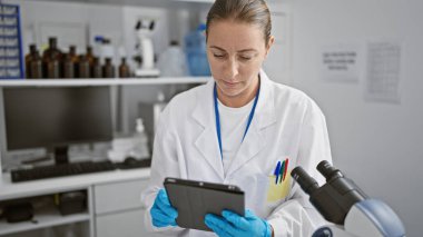 Hızlı tempolu laboratuvar ortamında dokunmatik bir dokunmatik ped kullanarak çığır açan biyoloji deneyine odaklanmış genç sarışın kadın bilim adamı..