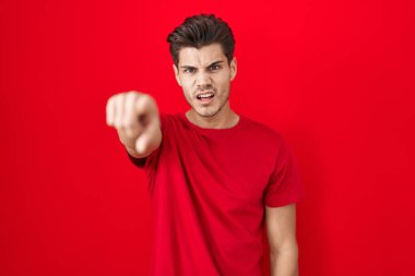 Kırmızı arka planda dikilen İspanyol genç adam kameraya kızgın ve sinirli olduğunu gösteriyor. 