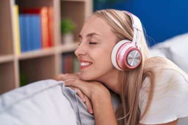 Genç sarışın kadın evdeki kanepede oturmuş müzik dinliyor.