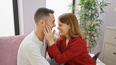 Sıcak bir yatak odasında gülümseyen ve kucaklaşan sevgi dolu bir çift..