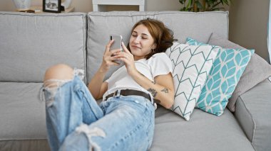 Genç kadın evde koltukta yalan smartphone kullanarak