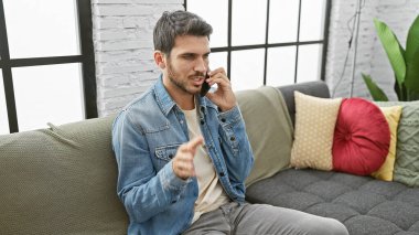 Modern bir oturma odasındaki bir kanepede otururken, şık giyinmiş yakışıklı bir İspanyol, akıllı bir telefonla konuşuyor..