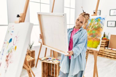 Beyaz kadın sanatçı gülümsüyor. Sanat stüdyosuna özgüvenli bakıyor.