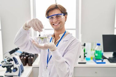 Young caucasian man scientist holding test tube with plant at laboratory