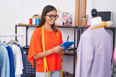 Genç, güzel İspanyol kadın terzi dükkanında dokunmatik ped kullanarak gülümsüyor.