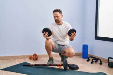 Genç beyaz adam gülümsüyor. Spor merkezinde spor yapmak için barlara ve disklere hazırlanıyor.