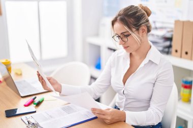 Genç sarışın iş kadını ofiste dizüstü bilgisayar okuyarak çalışıyor.