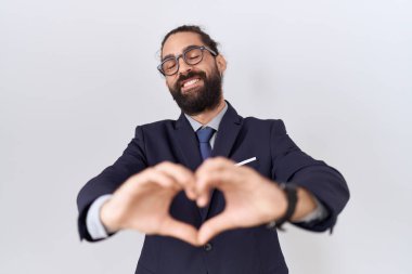 Hispanic man with beard wearing suit and tie smiling in love doing heart symbol shape with hands. romantic concept. 