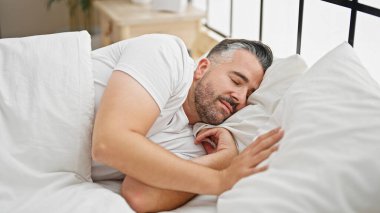 Gri saçlı adam yatakta uzanıyor, yatak odasında uyuyor.