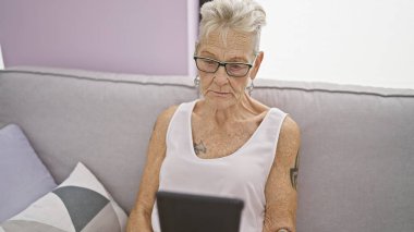 Ciddi, gri saçlı, teknolojiye çok düşkün, rahat bir şekilde koltuğunda oturmuş interneti tarayan dokunmatik bir cihaz kullanıyor, modern, olgun bir yaşam tarzını somutlaştırıyor.