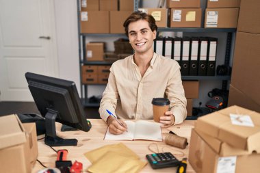 Young caucasian man ecommerce business worker writing on notebook drinking coffee at office