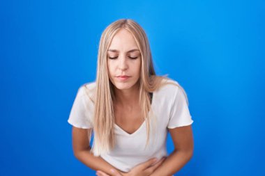 Mavi arka planda, hazımsızlık, acı veren hastalıklar yüzünden elleri karnında duran beyaz bir kadın. Ağrı kavramı. 