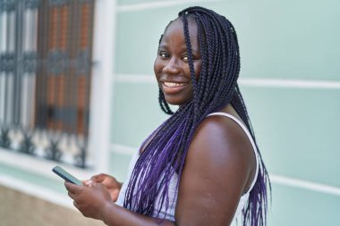 Afro-Amerikalı kadın sokakta akıllı telefon kullanarak kendine güveniyor.