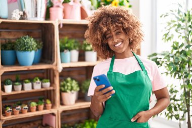 Çiçekçide akıllı telefon kullanarak gülümseyen Afrikalı Amerikalı kadın.
