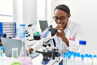 Laboratuvarda bilgisayar ve mikroskop kullanan Afrikalı Amerikalı kadın bilim adamı.