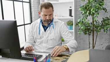 Parlak bir klinikte bilgisayar başında çalışan gri saçlı, olgun bir İspanyol doktor..