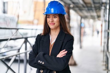 Güzel İspanyol kadın mimar gülümsüyor. Kollarını kavuşturup caddede duruyor.