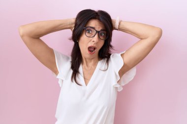 Orta yaşlı İspanyol kadın, günlük beyaz tişört ve gözlük takıyor. Deli gibi gözlük takıyor ve elleri başının üstünde korkmuş ve ağzı açık olan şok geçirmekten korkuyor. 